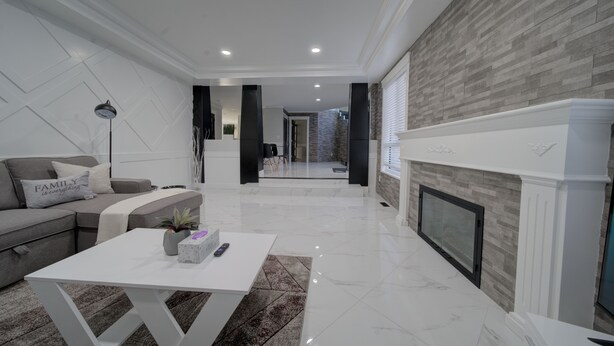 A modern living room with a white sofa, a coffee table, and a fireplace. - 6 bdrm home w pool/hot tub/pool table/bar/kareoke (Surrey)