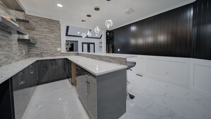 A modern kitchen with a marble countertop, built-in appliances, and a dark wooden accent wall. - 6 bdrm home w pool/hot tub/pool table/bar/kareoke (Surrey)
