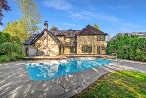 Une maison à deux étages avec une piscine, entourée d’une pelouse bien entretenue et d’arbres.