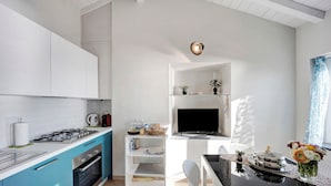 A modern kitchen with a gas stove, oven, and blue cabinets. There is a dining area with a table and chairs, and a TV mounted on the wall. - Vacation Apartment in the Historic Center with Sea View and Shared Garden (Bordighera)