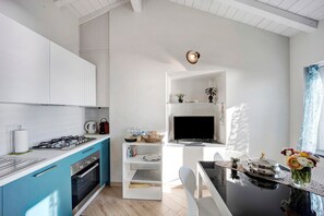 A modern kitchen with a gas stove, oven, and blue cabinets. There is a dining area with a table and chairs, and a TV mounted on the wall.