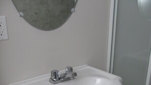 A bathroom with a white sink, a mirror above it, and a shower area to the right. - Furnished house in Geraldton (Geraldton)