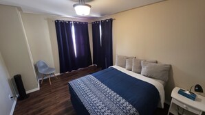 A bedroom with a bed, a chair, a bedside table, and a window with curtains. - Furnished house in Geraldton (Geraldton)