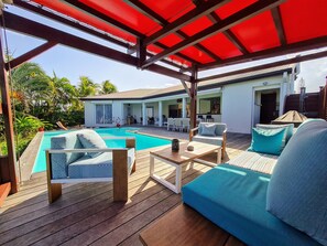 A covered outdoor area with a pool, wooden deck, and outdoor furniture.