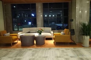 A modern hotel lobby with a sofa set, two round coffee tables, and a large window offering a view of the cityscape at night. - Shuang Yi Hotel (Huizhou)