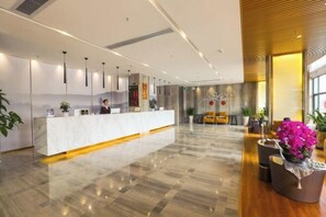 Un moderno vestíbulo de hotel con una recepción, zona de estar y plantas decorativas.