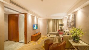 A hotel room with a TV, sofa, armchair, coffee table, and a plant. - Shuang Yi Hotel (Huizhou)