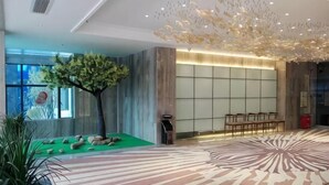 A lobby with a green carpet, a tree sculpture, a patterned floor, and a seating area. - Shuang Yi Hotel (Huizhou)