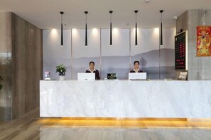 A reception desk with three monitors, a plant, and a wall-mounted sign. - Shuang Yi Hotel (Huizhou)