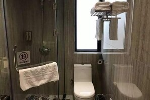 Un baño con ducha acristalada, inodoro y toallero con toallas.