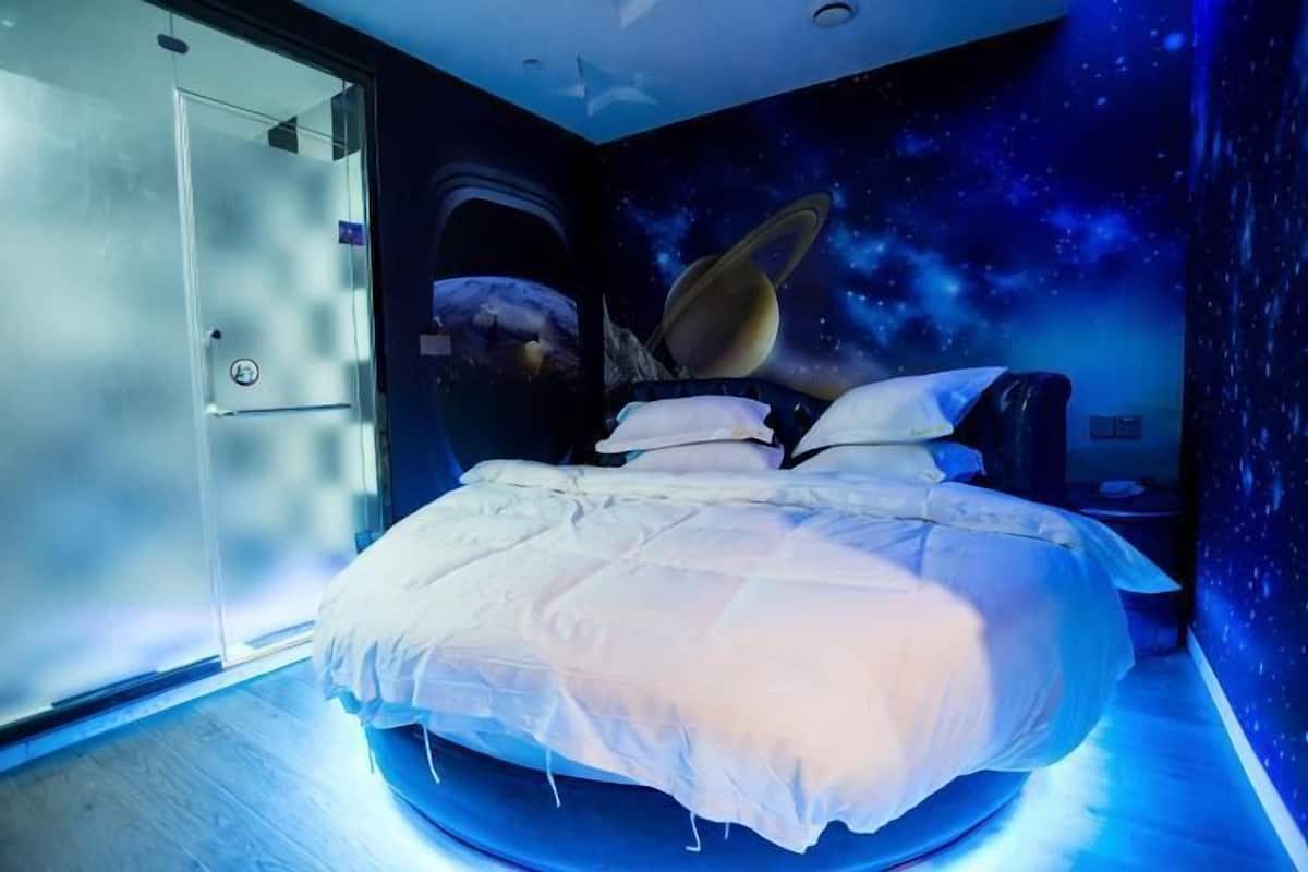 Un dormitorio con una cama en el centro, una puerta a la izquierda y un mural de espacio en la pared.