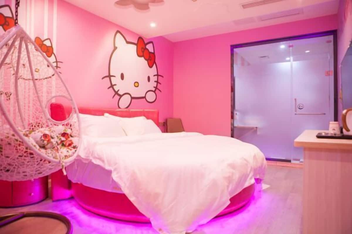Una habitación con decoración rosa, una cama, un adorno de pared con temática de Hello Kitty y una silla colgante.