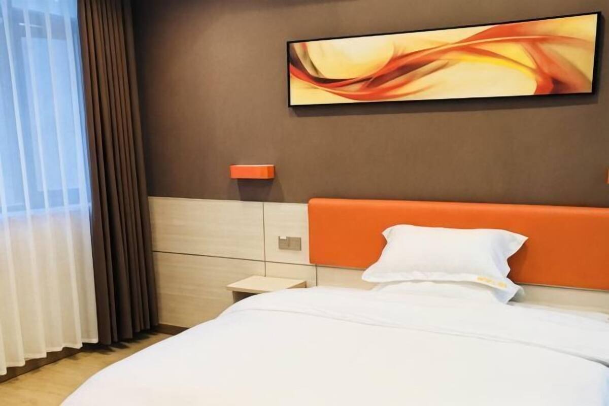 Una habitación de hotel con cama, mesita de noche, un cuadro colgado en la pared y ventana con cortinas.