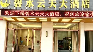 Entrada de hotel con letrero, puertas de vidrio y mostrador de recepción.
