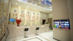 Zona de recepción de un hotel con mostrador de mármol, tres taburetes de bar, una pantalla digital y un techo decorativo.