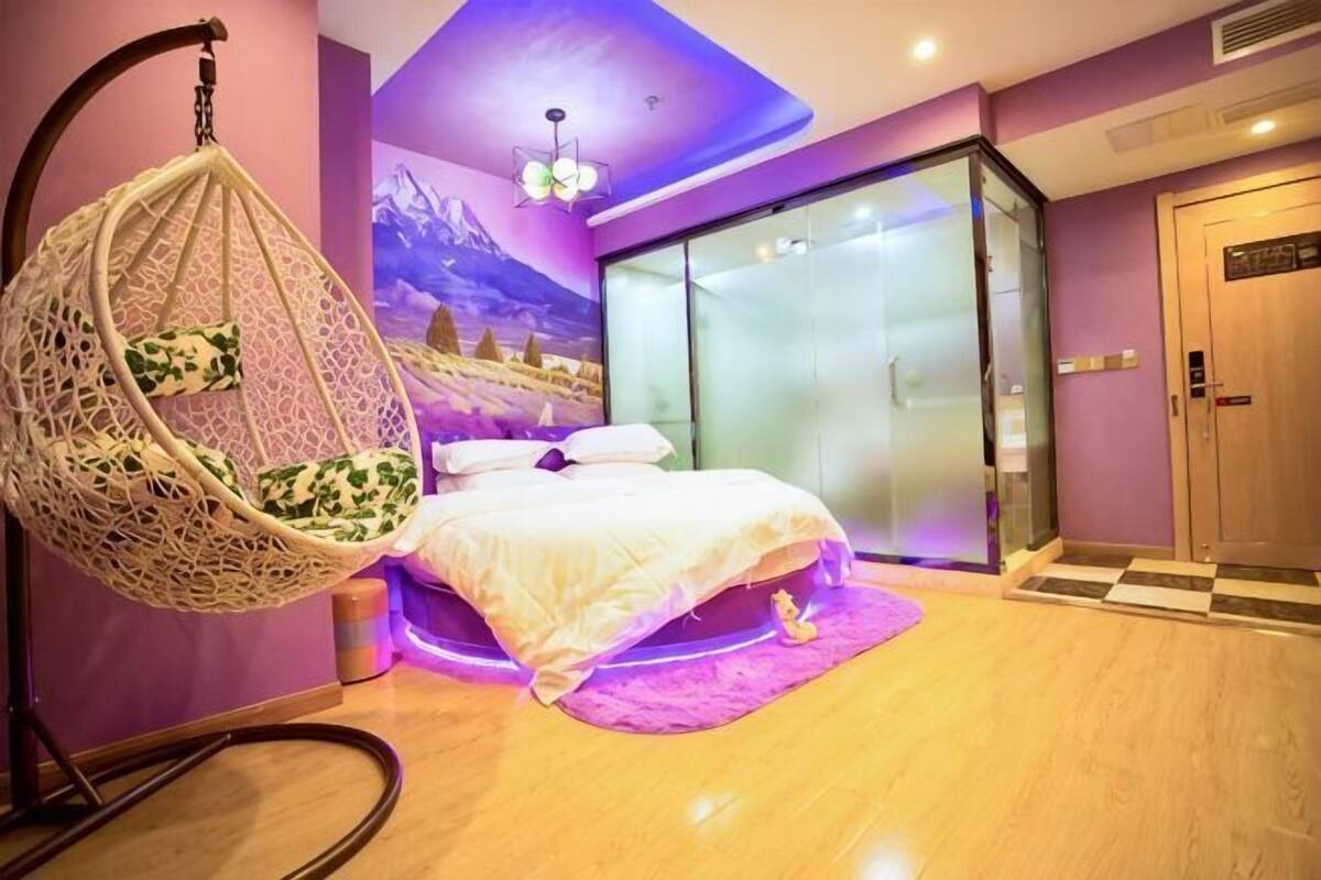 Un dormitorio con una silla colgante, una cama, un puerta de vidrio y una pared morada.