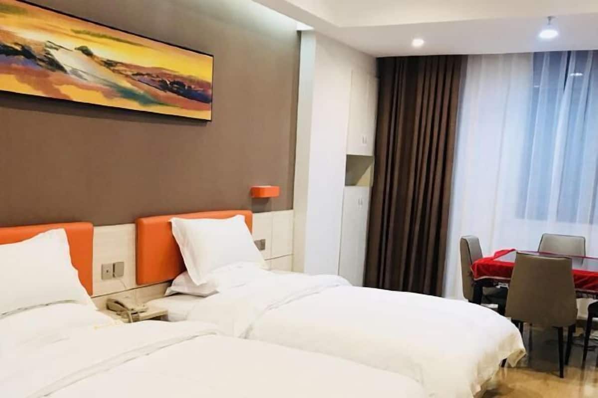 Habitación de hotel con dos camas, un cuadro en la pared, una mesa de comedor con sillas y una ventana con cortinas.