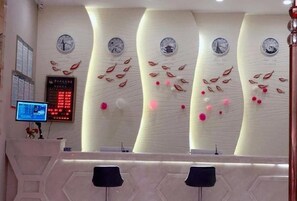 Un área de recepción con diseño moderno, que presenta una pared curva con relojes y elementos decorativos. Hay un panel de visualización digital y un mostrador de recepción con sillas.