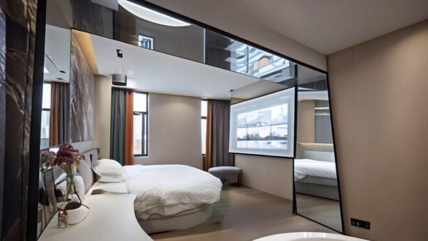 A modern hotel room with a large bed, a sitting area with a sofa and a coffee table, a large mirror, and a view of the city through the window. - Xiyue Ruixuan Hotel (Jingdezhen)