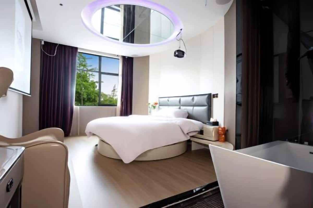 Moderni hotellihuone, jossa on pyöreä sänky, työpöytä, tuoli, suuri ikkuna ja pyöreä kattovalaisin.
