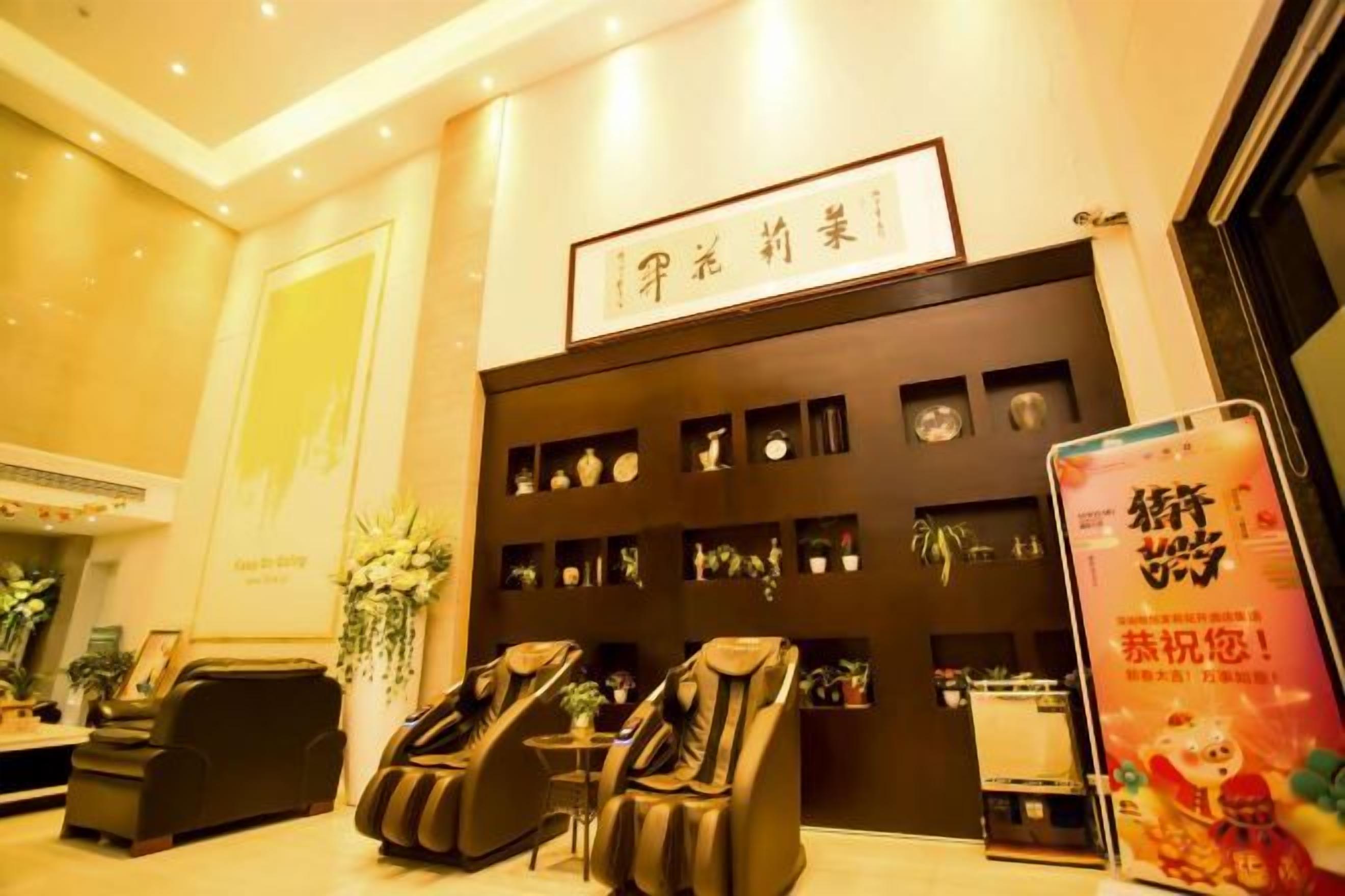 A reception area with a reception desk, two massage chairs, a wall with shelves displaying items, and a poster on the wall.