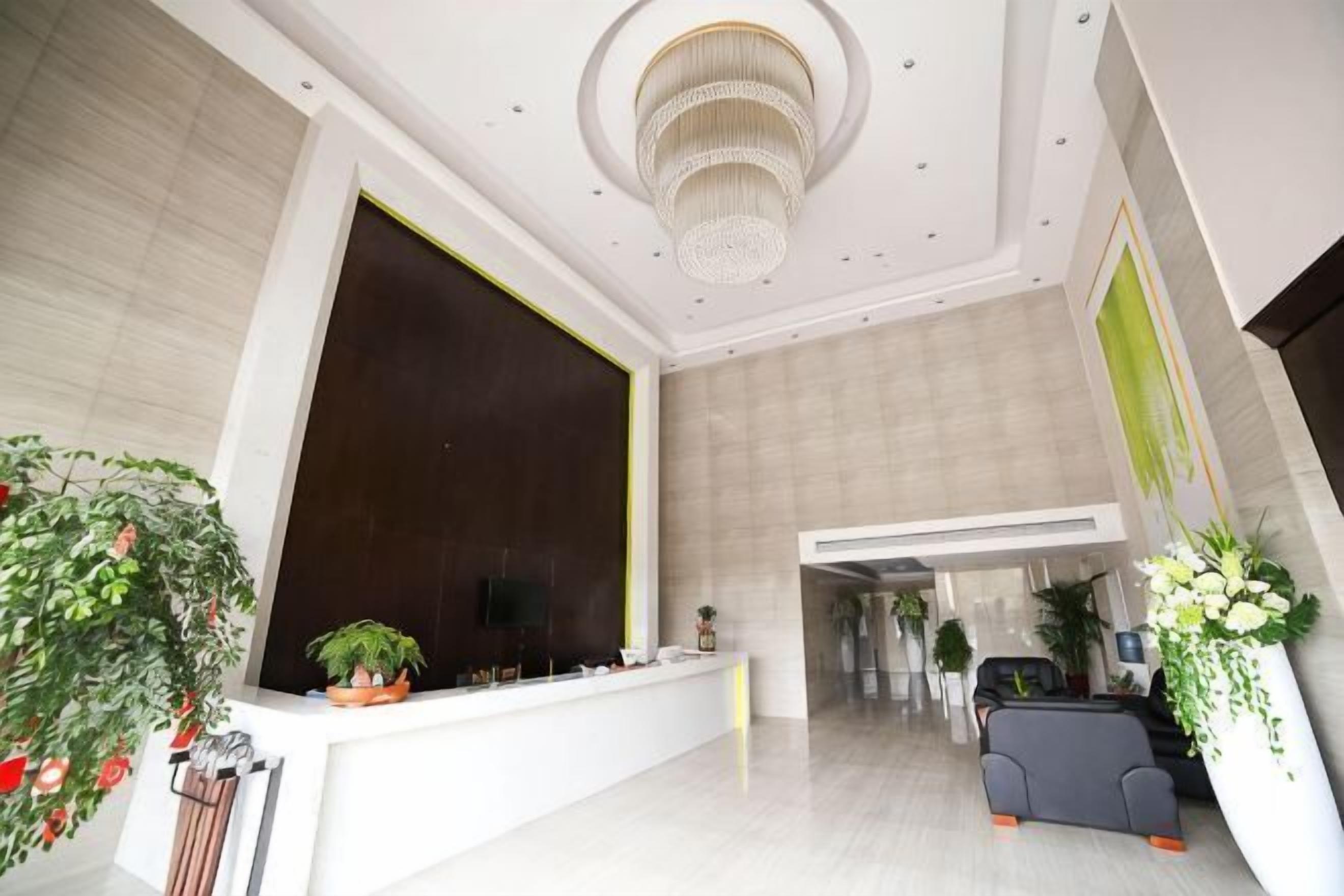 A spacious lobby with a reception desk, a chandelier, and potted plants.