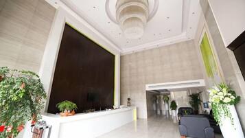 A spacious lobby with a reception desk, a chandelier, and potted plants.