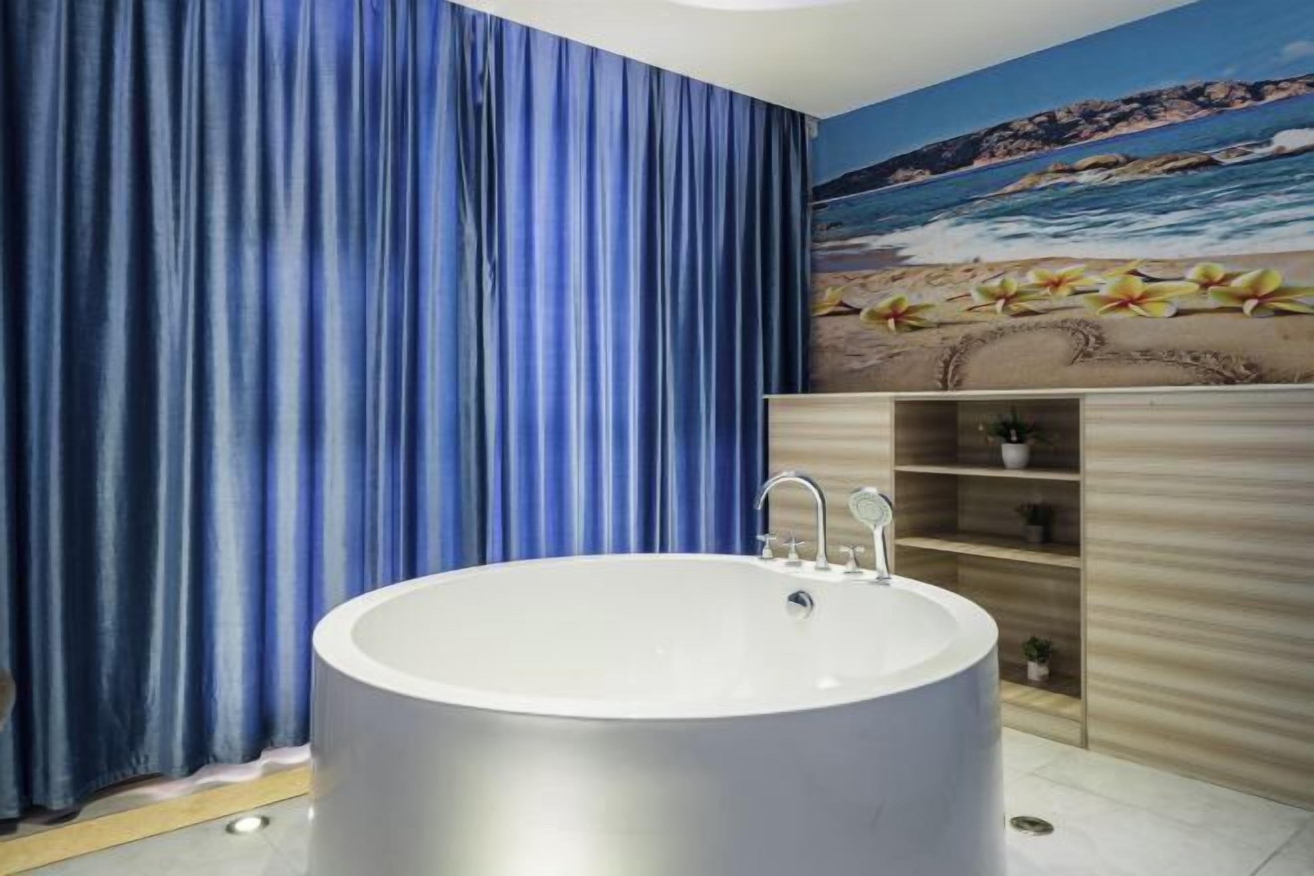 A bathroom with a large bathtub, blue curtains, a wooden vanity, and a beach mural on the wall.