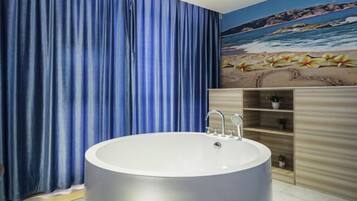 A bathroom with a large bathtub, blue curtains, a wooden vanity, and a beach mural on the wall.