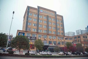 A multi-story hotel with a central entrance, surrounded by parked cars and trees.