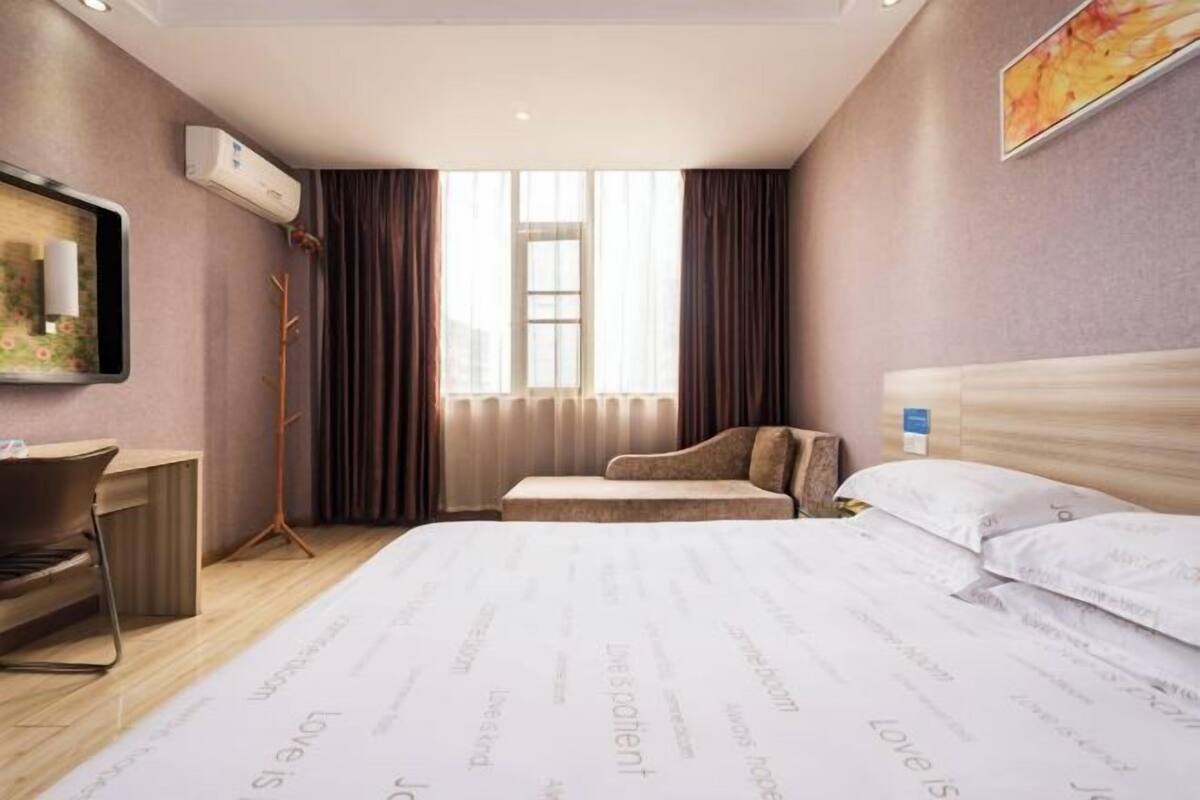 Habitació d'hotel amb un llit, escriptori, cadira, làmpada de peu i una finestra amb cortines.