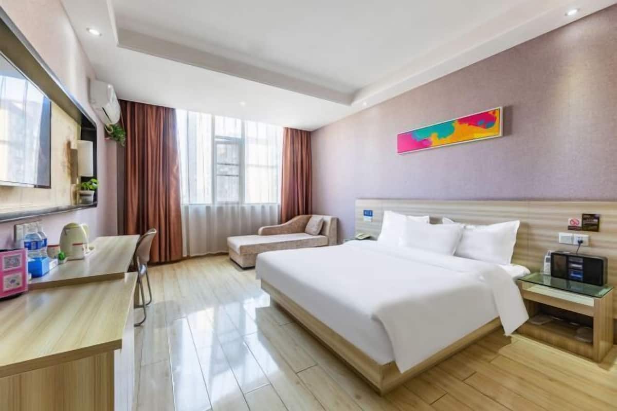 Una habitació d'hotel amb un llit gran, un escriptori amb una cadira, un televisor i una obra d'art colorida a la paret.