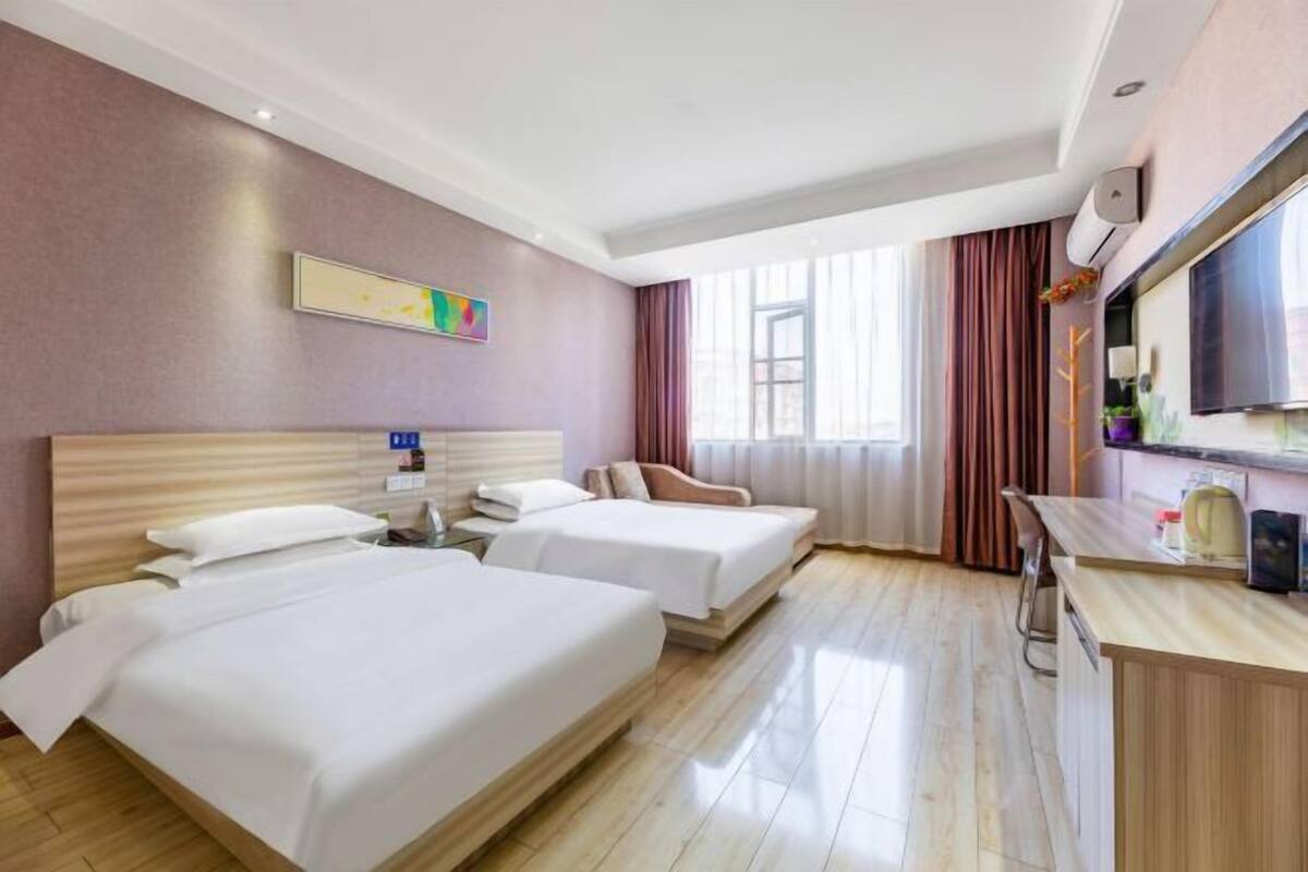Habitació d'hotel amb dos llits, una taula de treball, televisió i finestra amb cortines.