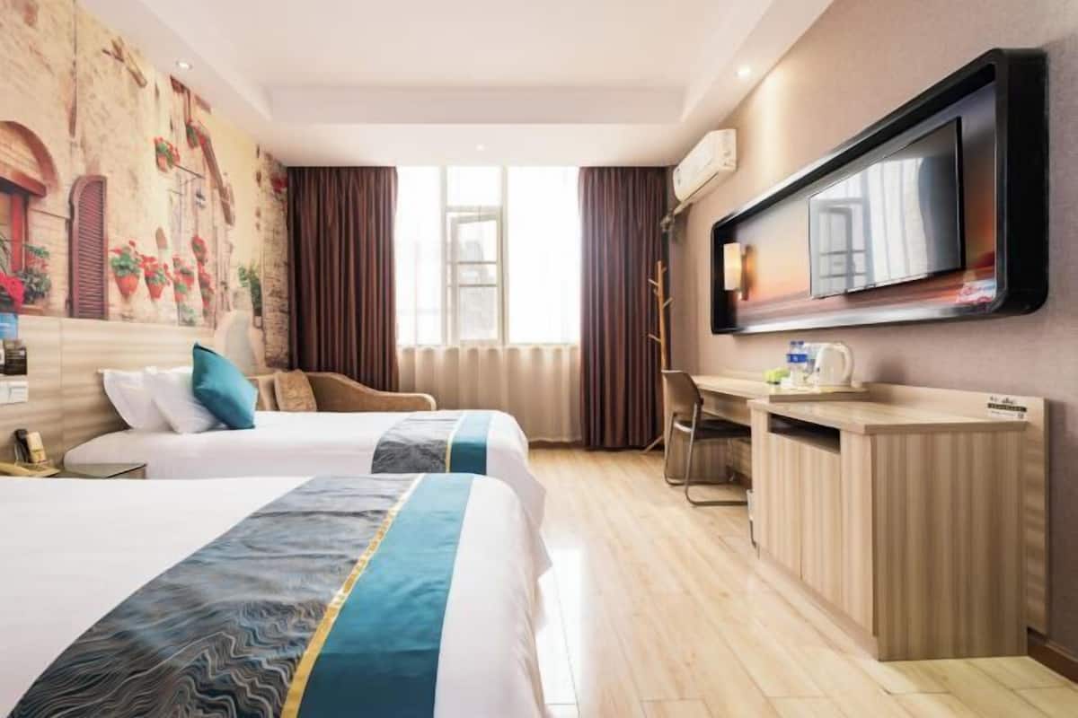 Habitació d'hotel amb dos llits, televisió, escriptori i un mural a la paret.