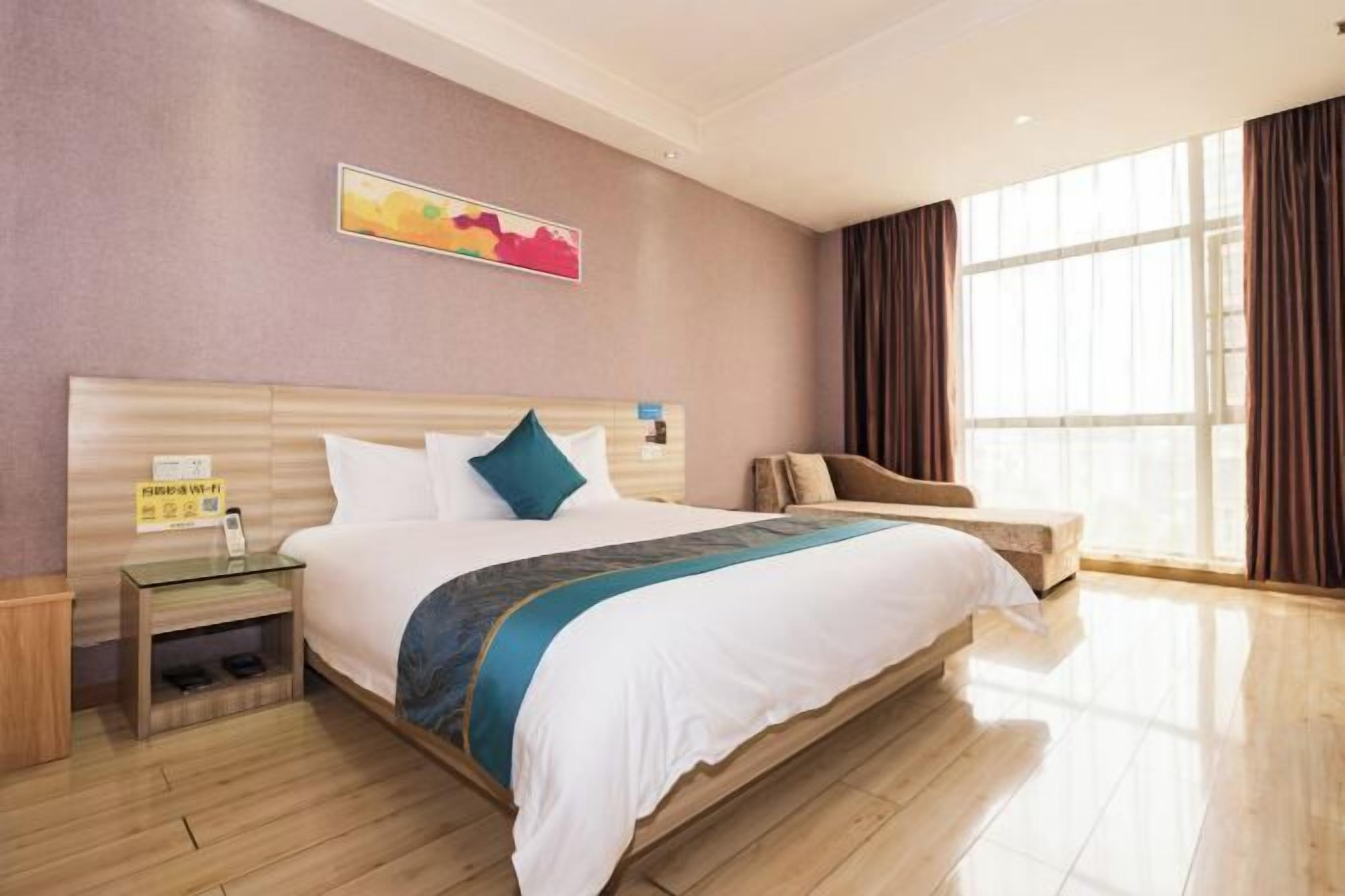 Una habitación de hotel con cama, mesita de noche y ventana con cortinas.