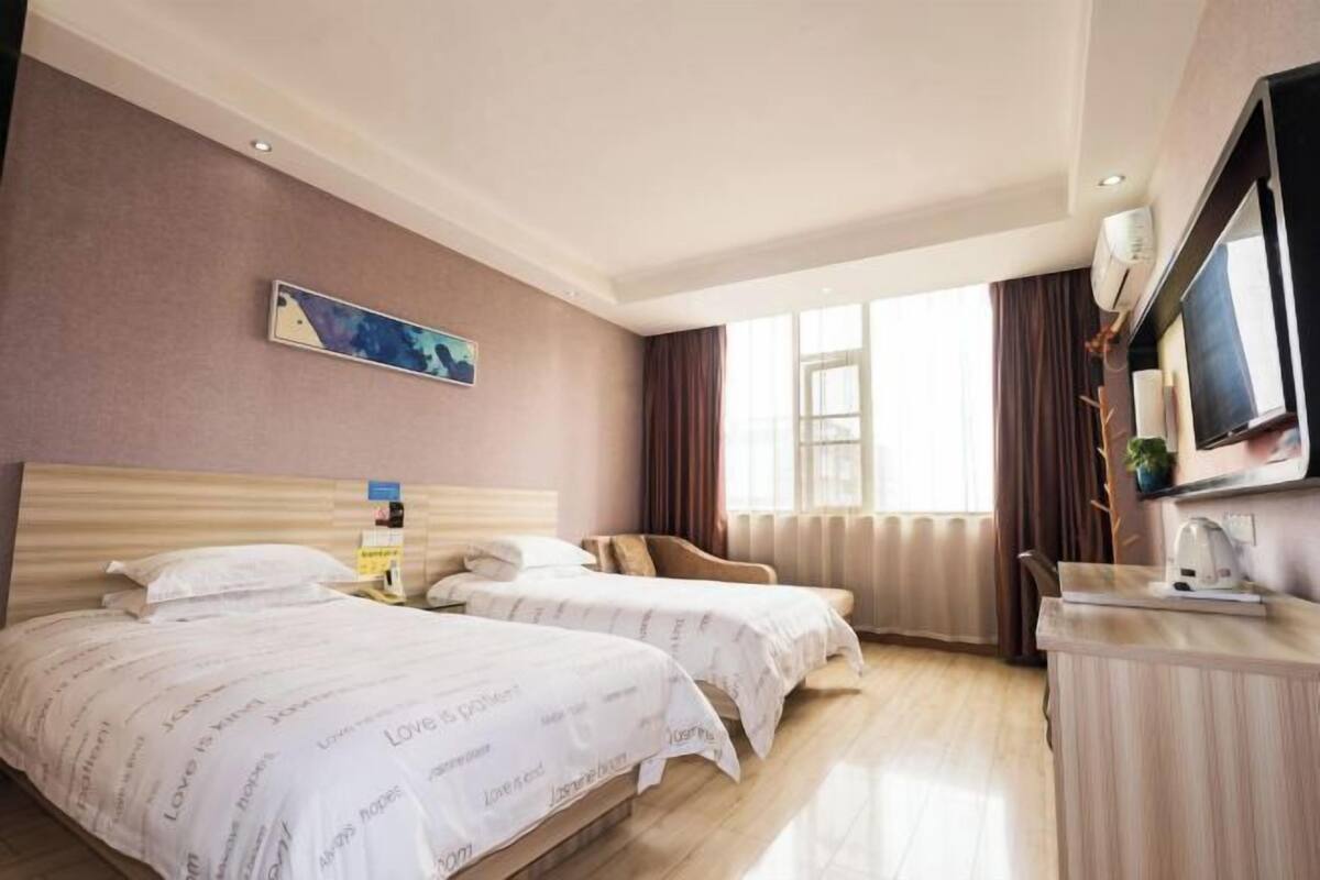 Habitació d'hotel amb dos llits, televisió, escriptori i finestra amb cortines.