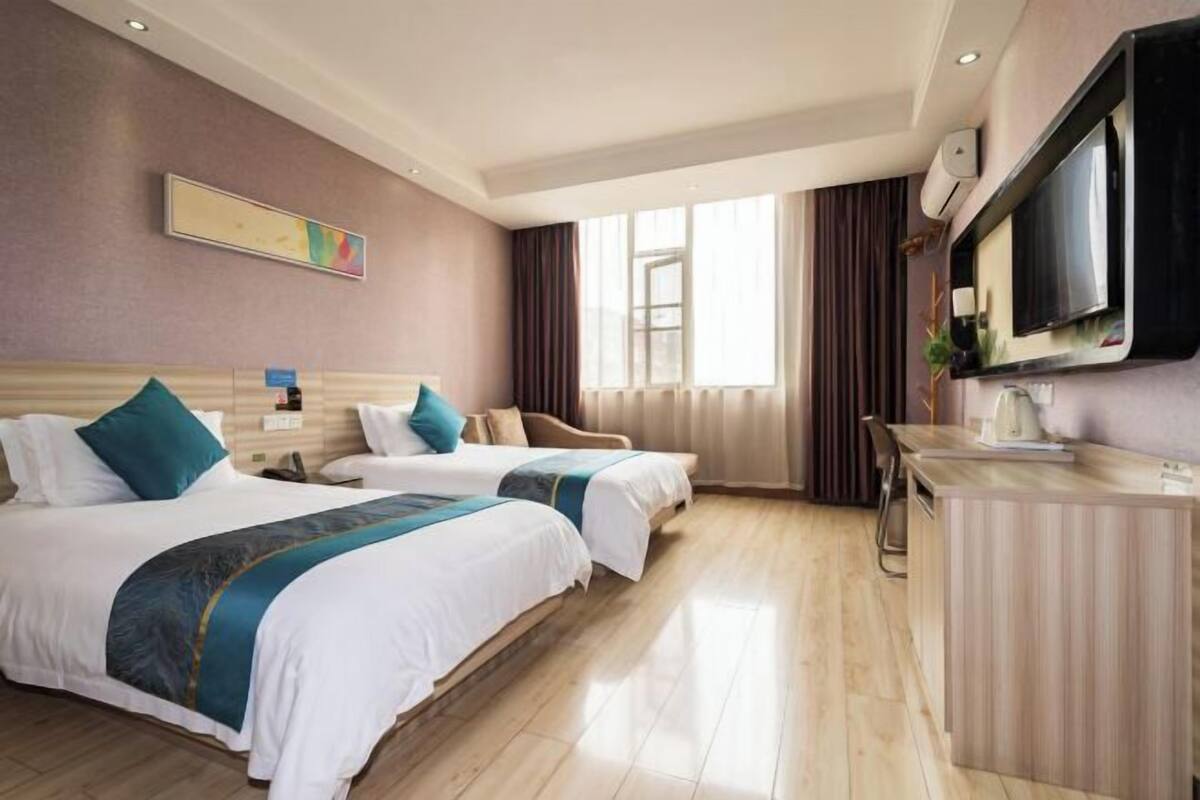 Habitació d'hotel amb dos llits, una taula de treball, una televisió i una finestra amb cortines.
