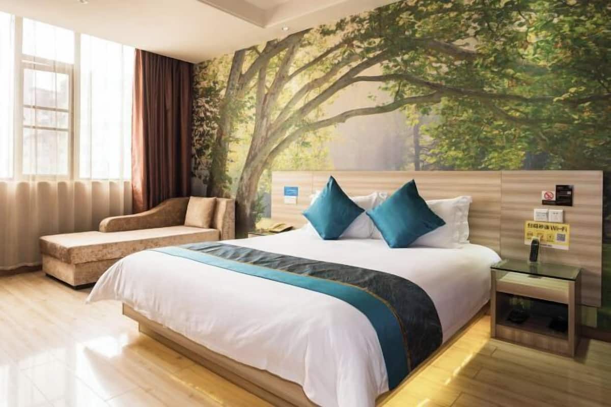 Habitació d'hotel amb un llit gran, un sofà, una tauleta de nit i un mural a la paret.