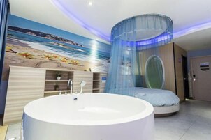 Un baño moderno con una bañera grande, un mural con temática playera y una ventana circular única.