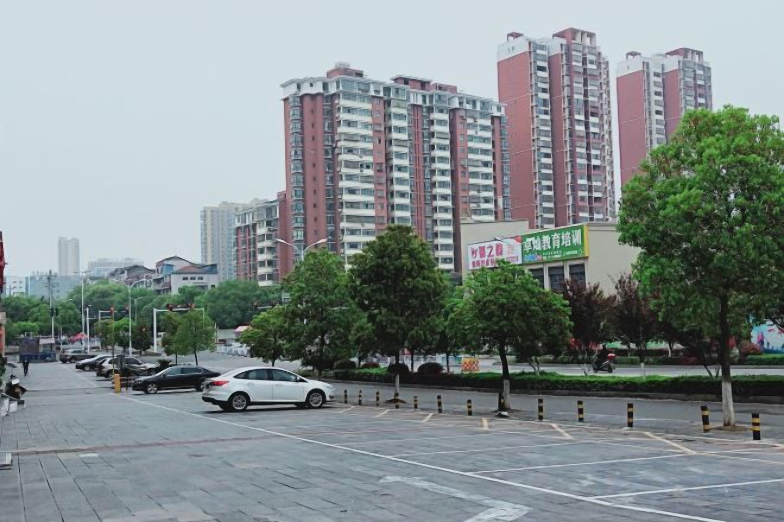 A parking lot with cars, trees, and a building with a green sign.