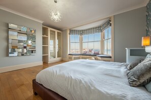 A bedroom with a large bed, a built-in wardrobe, a seating area by a window, and a decorative mirror on the wall. - Boycott House, Cromer, Norfolk (Cromer)