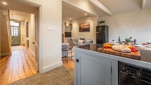 A modern kitchen with a wooden countertop, a dishwasher, and a dining area with a sofa and a table. - Norfolk House, Heacham, Norfolk (Heacham)