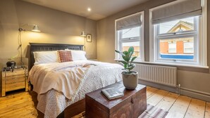 A bedroom with a bed, bedside lamps, a radiator, a window with blinds, and a view of a building outside. - Norfolk House, Heacham, Norfolk (Heacham)