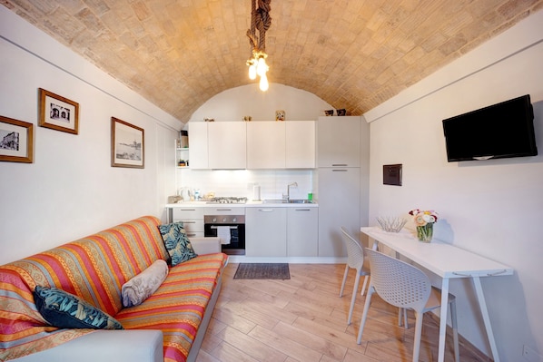 A compact living space with a sofa, a dining table, a TV, and a kitchen area.