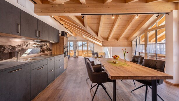 A modern kitchen with wooden beams, a dining area with a large table and chairs, and a view through large windows. - Holiday Apartment "Susi" in a New Building with View of the Zugspitze, 2 Balconies & Wi-Fi (Farchant)