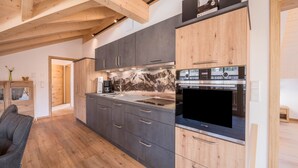 A modern kitchen with wooden beams, grey cabinets, a large stove, and a black TV. - Holiday Apartment "Susi" in a New Building with View of the Zugspitze, 2 Balconies & Wi-Fi (Farchant)