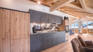 A modern kitchen with wooden cabinets and a large island, a dining area with a table and chairs, and a view of the outdoors. - Holiday Apartment "Susi" in a New Building with View of the Zugspitze, 2 Balconies & Wi-Fi (Farchant)