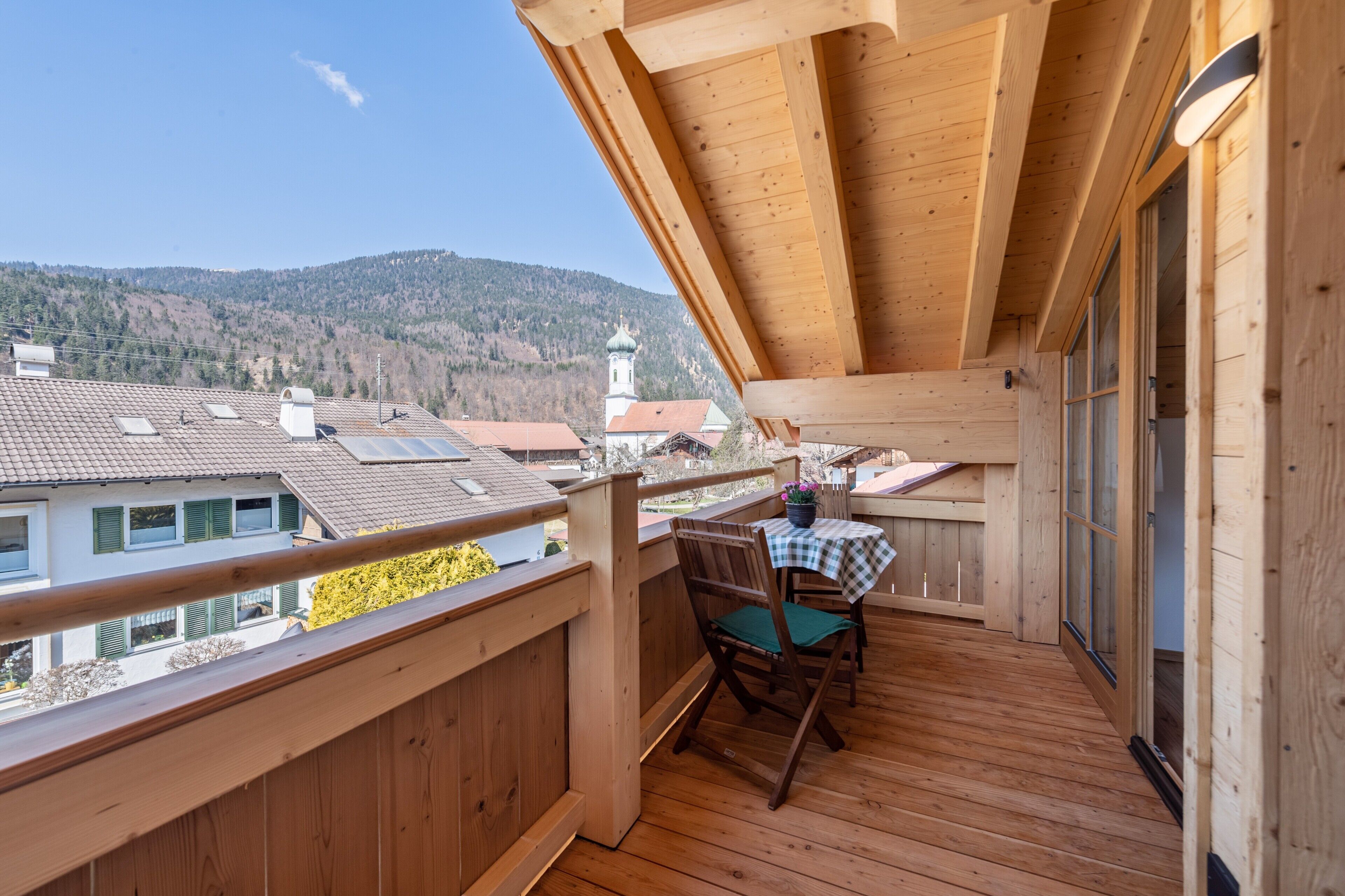 Un balcón de madera con una mesa y sillas, con vista a un pueblo y montañas.