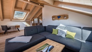 A modern loft-style room with a large sectional sofa, a wooden coffee table, a desk, and a skylight. - Holiday Apartment "Susi" in a New Building with View of the Zugspitze, 2 Balconies & Wi-Fi (Farchant)