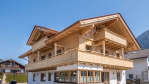 A two-story wooden chalet with balconies, large windows, and a mountain backdrop. - Holiday Apartment "Susi" in a New Building with View of the Zugspitze, 2 Balconies & Wi-Fi (Farchant)
